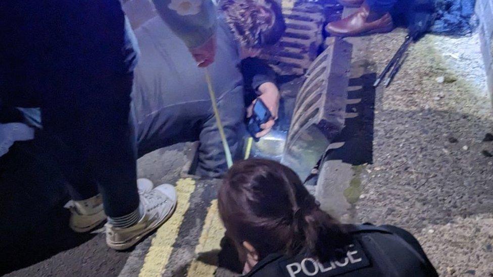 People trying to rescue ducklings in a drain