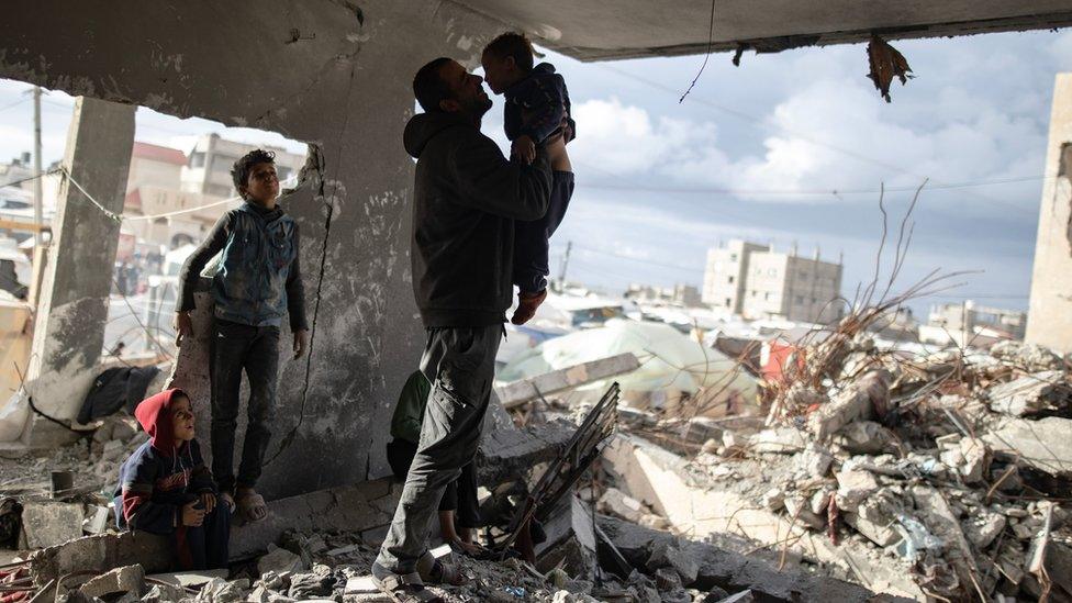 Displaced Palestinian Muhammad Al-Durra, 41, plays with his children at the destroyed house they took shelter in, in the city of Rafah