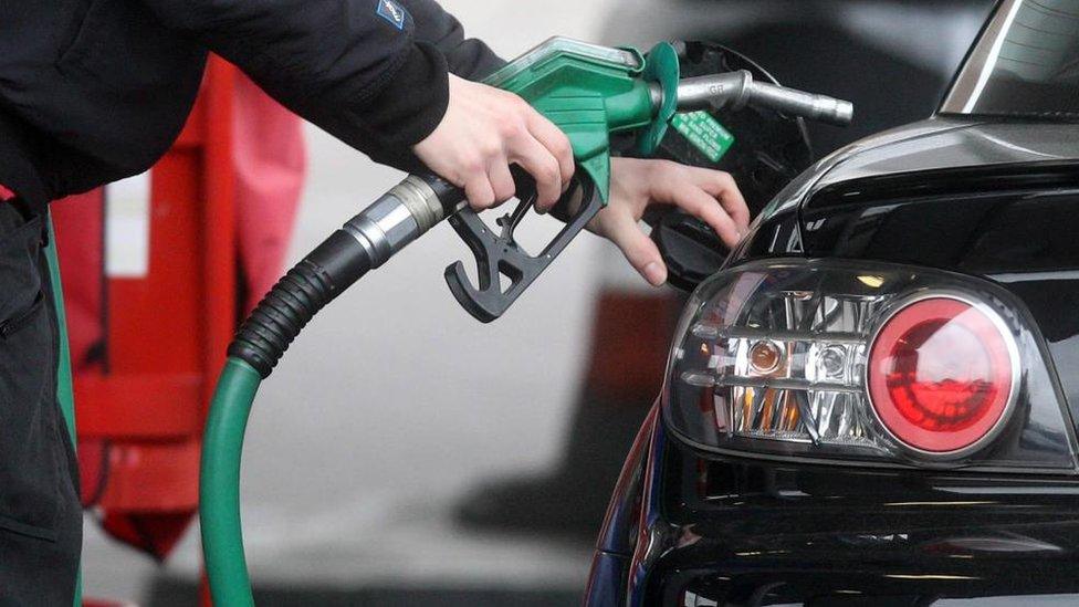 A man holds a petrol pump in one hand and opens the petrol cap of his car with the other