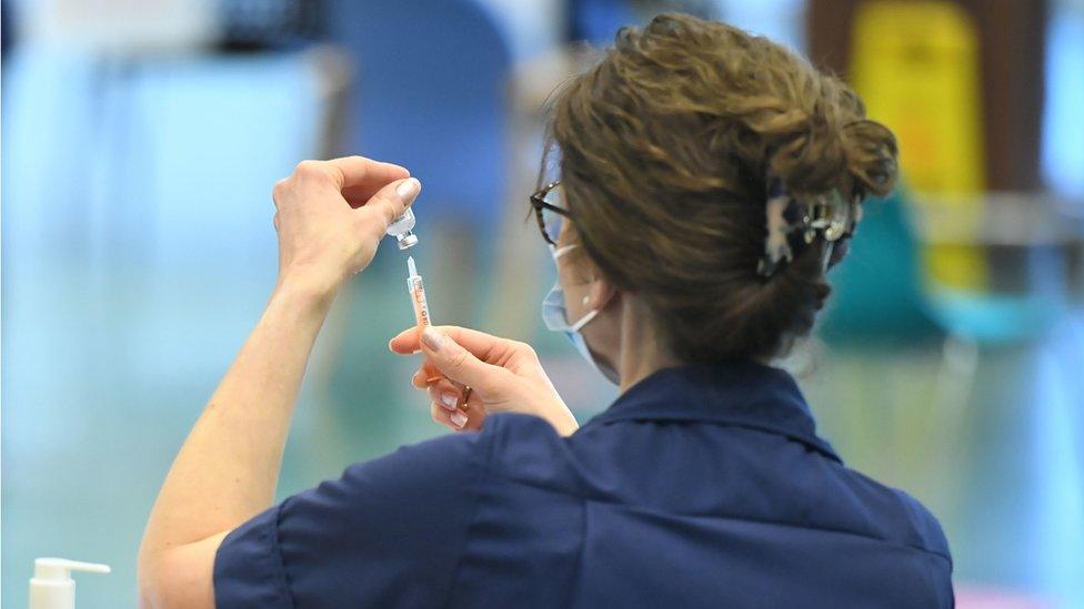 A woman holding up a vaccine vial