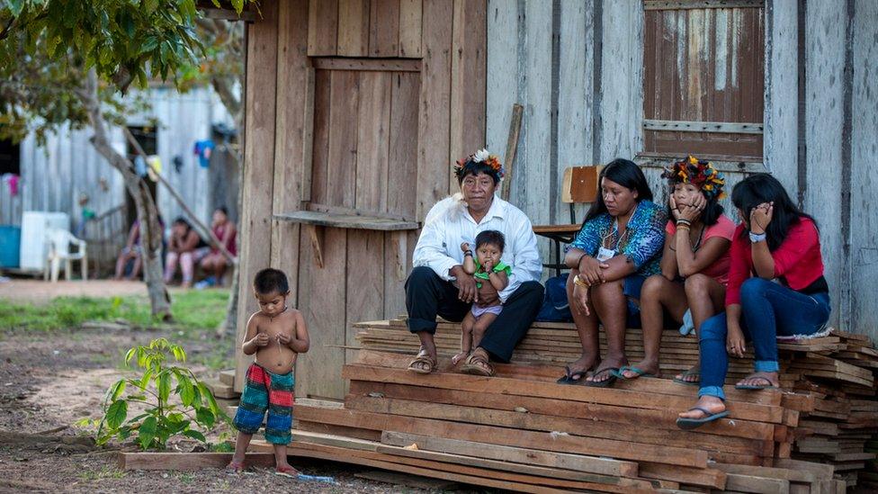 A group of members of the Cinta Larga sit in front of a house