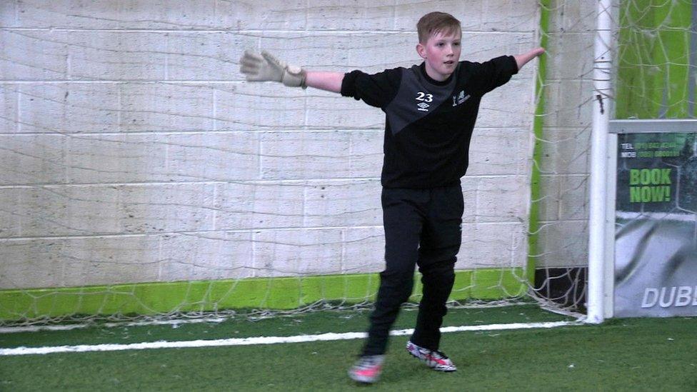 Boy standing in football goal with arms outstretched