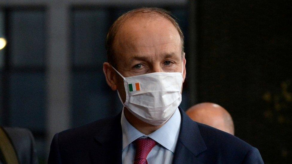 Taoiseach Micheál Martin wearing a face covering with an Irish flag attached