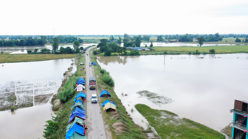 A humanitarian aid car drives down a narrow road over a swollen river in western Napal