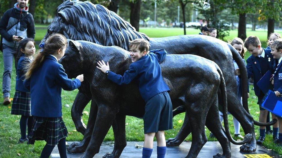 Children from a local school embrace two lion sculptures