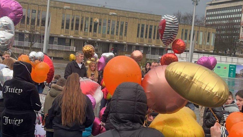 People holding balloons and gathered in a public square