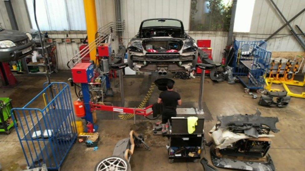 A car on a workshop ramp being stripped of parts