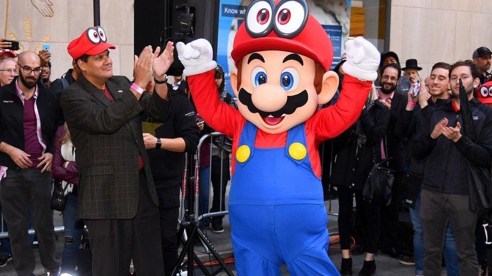 A person wearing a Mario costume lifts their hands above their head triumphantly as the crowd cheers.