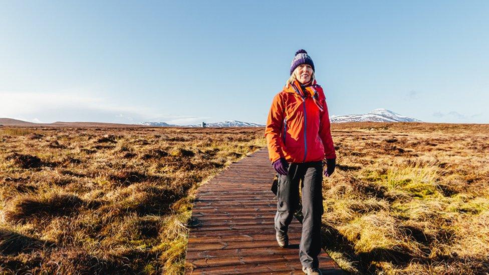 Woman walking over wooden path through peat bog