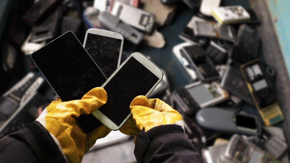 Phone waste, hands holding three phones in the foreground