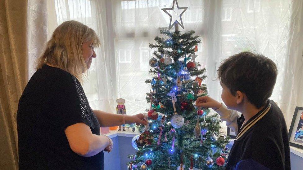 Mother and son standing either side of a Christmas tree and hanging decorations on it