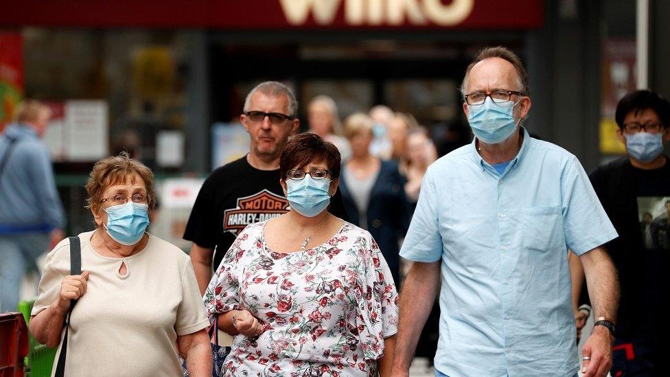 Shoppers, some wearing a face mask or covering due to the COVID-19 pandemic, walk past shops in Basingstoke, south west of London, on July 23, 2020, as consumers return to the shops following the continued lifting of novel coronavirus lockdown restrictions. - Facemasks will become compulsory in shops and supermarkets in England from Friday, after weeks of wrangling from ministers about their effectiveness.