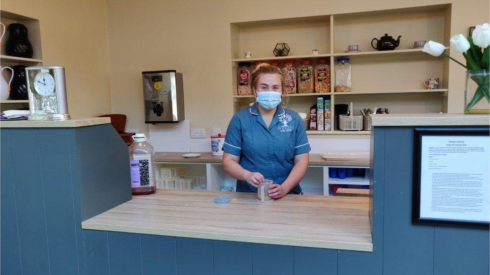 A care home worker behnid a counter wearing a mask