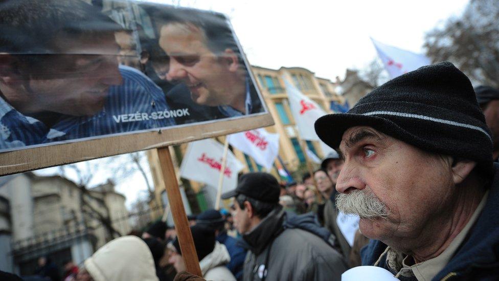 A participant at a 2103 rally holds a banner with a photo of Hungarian Prime Minister Viktor Orban (R) and senior Fidesz party member Zsolt Bayer (L)