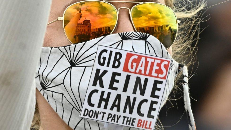 A protester wears a mask which says in German and English: "GIB GATES KEINE CHANCE DON'T PAY THE BILL"