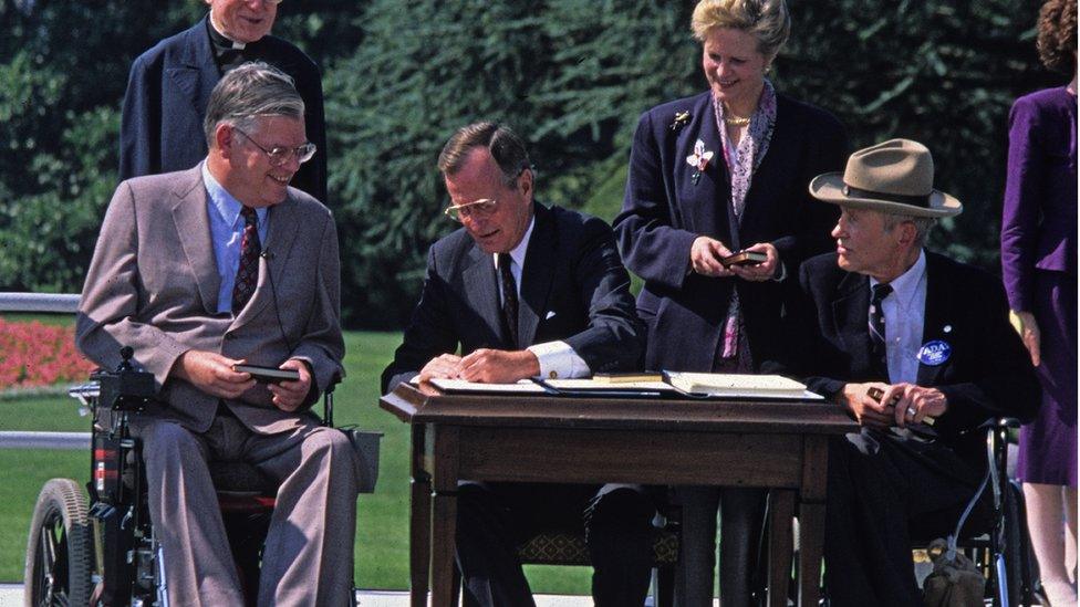 Pictured are, from left Chairman of the US Equal Employment Opportunity Commission Evan J Kemp Jr, Reverend Harold Wilke (1915 Ð 2003) (partly obscured), Bush, Chair of the National Council for Disabilities Sandra Parrino, and activist Justin Dart Jr (1930 - 2002)