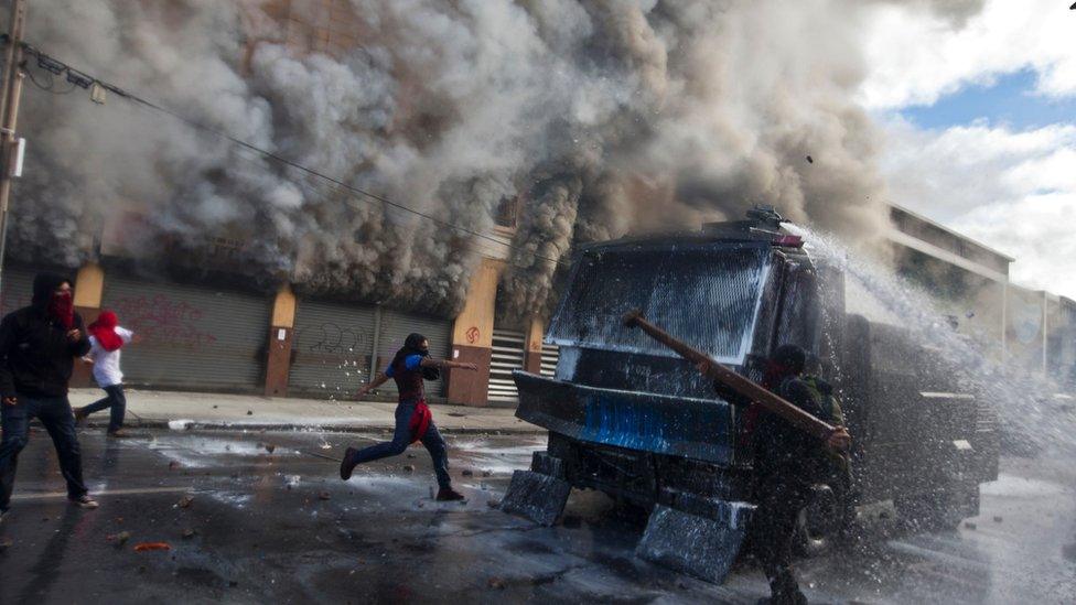 Masked protesters attack a police water canon in front of a burning pharamacy