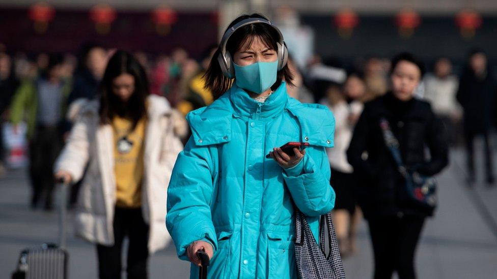 A woman wears a blue face mask as she wheels luggage