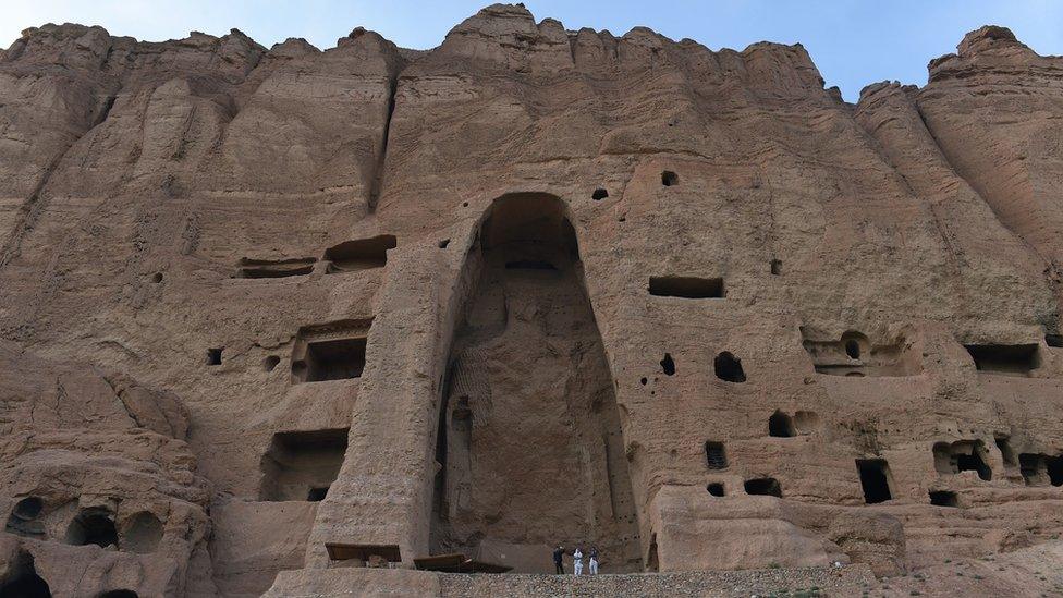 This file photograph taken on June 19, 2015, shows visitors as they walk in front of the empty site of two Buddha statues, which were destroyed by the Taliban, in Bamiyan