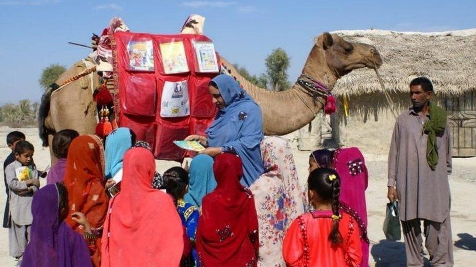 Children stand next to a camel that brought books