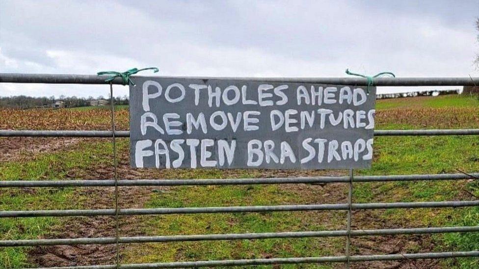 Potholes warning sign saying 'potholes ahead, remove dentures, fasten bra straps'