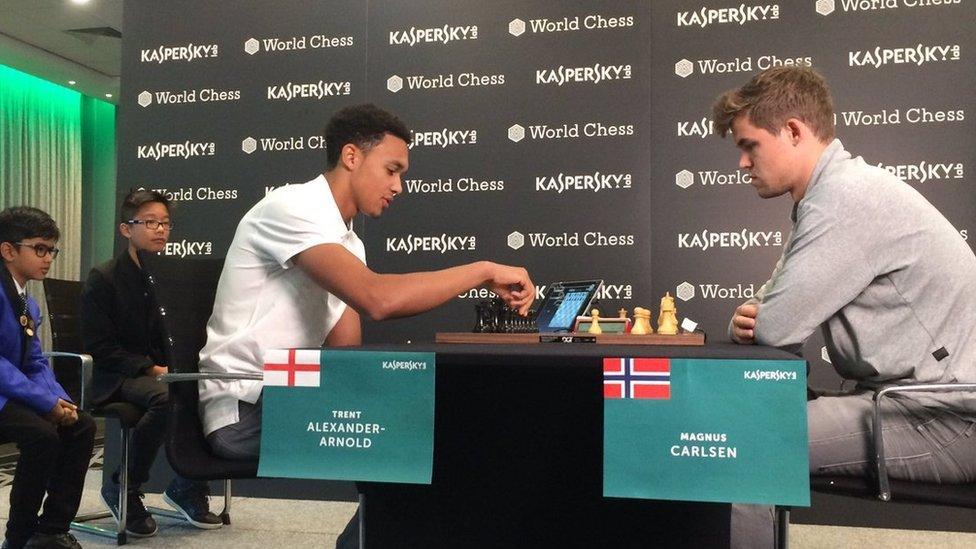 Trent Alexander-Arnold makes a chess move against champion Magnus Carlsen