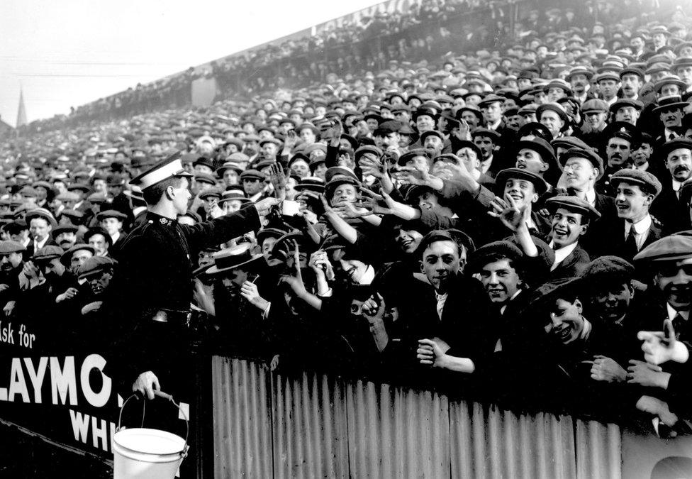 27th September 1913: An ambulance worker handing out water at a crowded football match between Tottenham Hotspur and Manchester City at White Hart Lane in London.