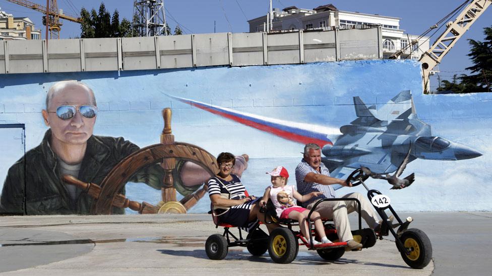 People pass a mural of Putin at the wheel of a ship