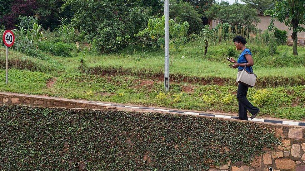 rwandan woman checks her mobile phone while walking up a slope