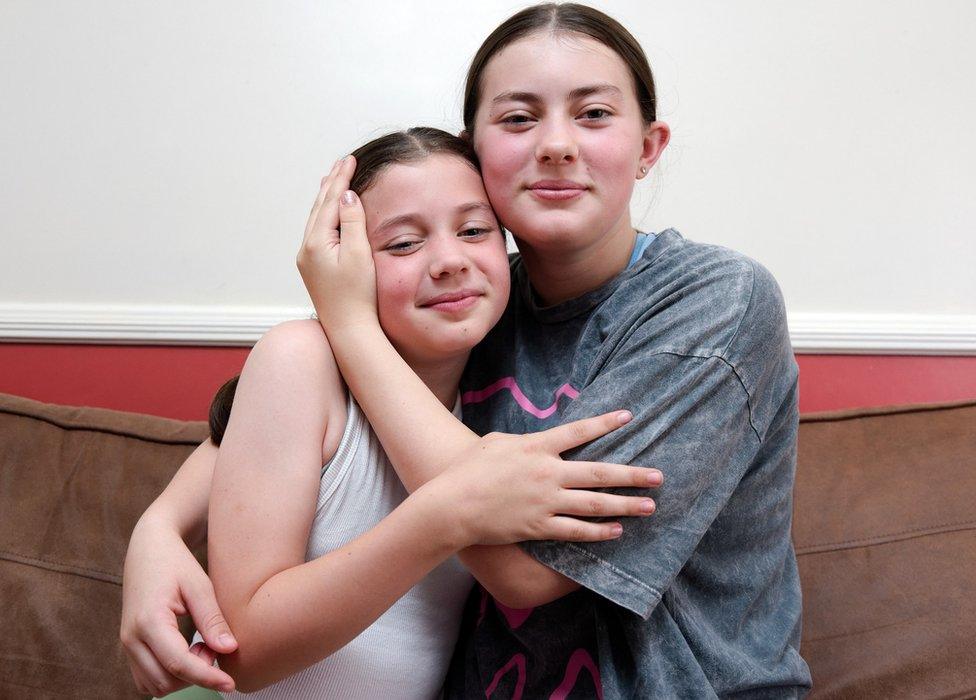 Sisters Flo and Grace shown sharing a hug on the couch of their home