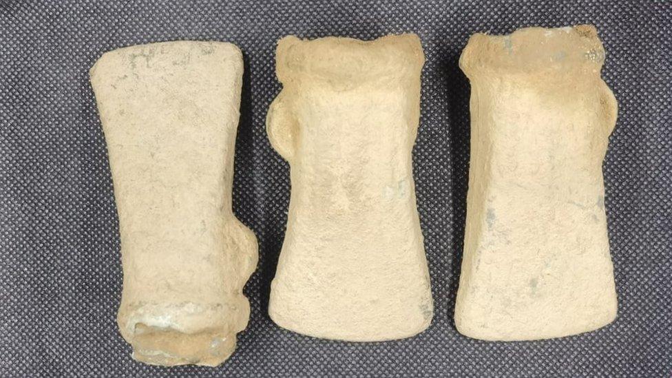 Three axe heads lie side by side on a grey mat