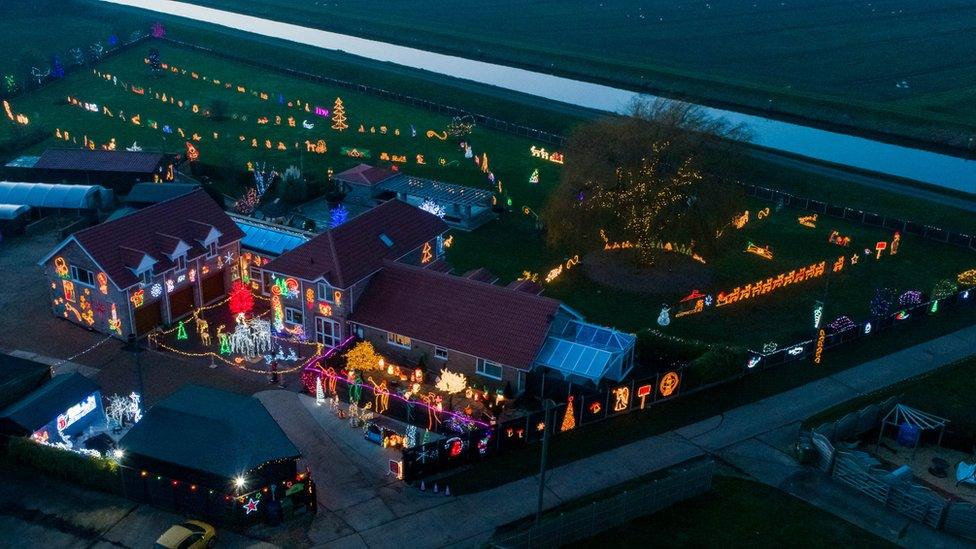 An aerial shot of a house and garden heavily decorated with Christmas lights and illuminated models.