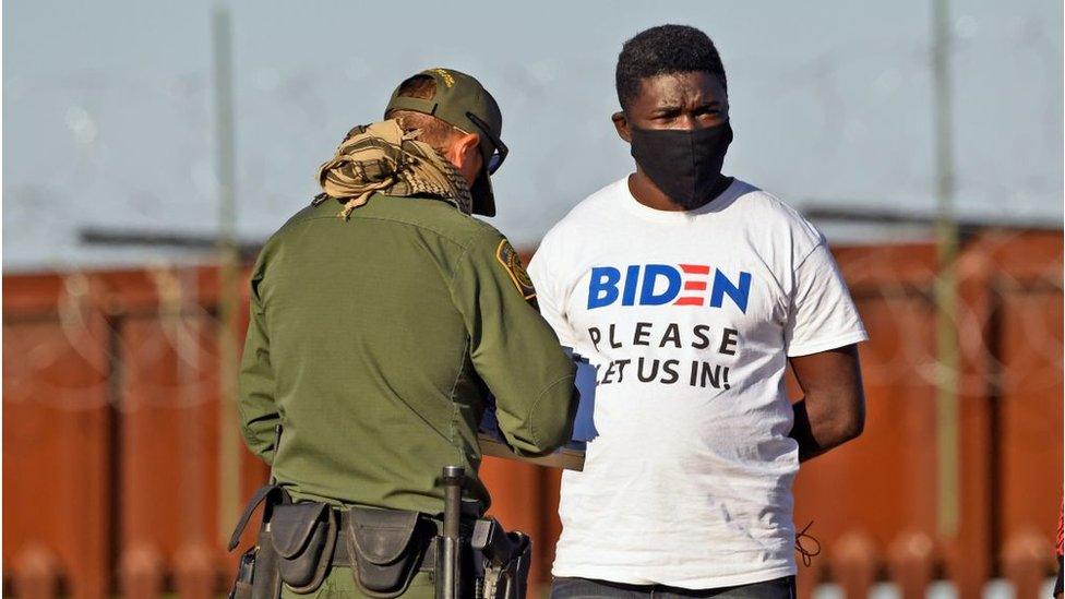 A man detained in Arizona wears a t-shirt saying "please let us in"