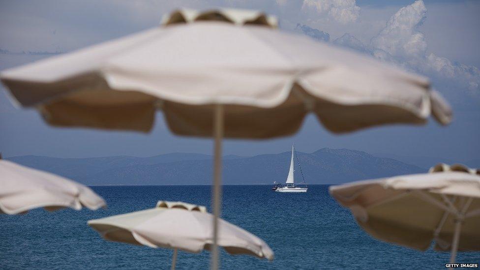 A yacht sails past parasols on the beach front on 3 June 2015 in Kos, Greece