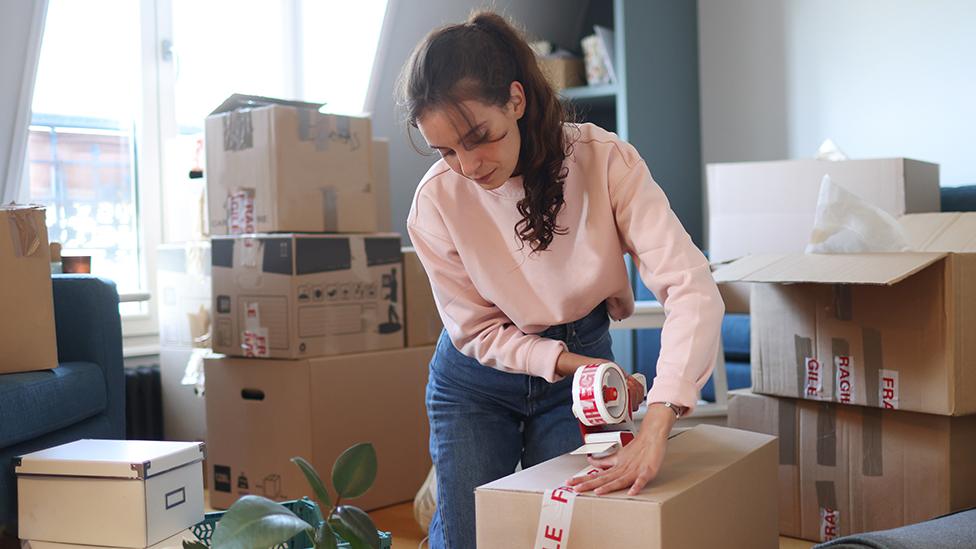 Woman packs boxes in room with window in background