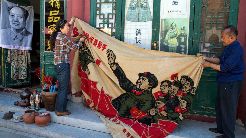 Vendors at a curio market in Beijing unfurl a banner from 1969 depicting former Chinese leader Mao Zedong, surrounded by Red Guards and the slogan "navigating the seas depends on the helmsman" on 16 May 2016