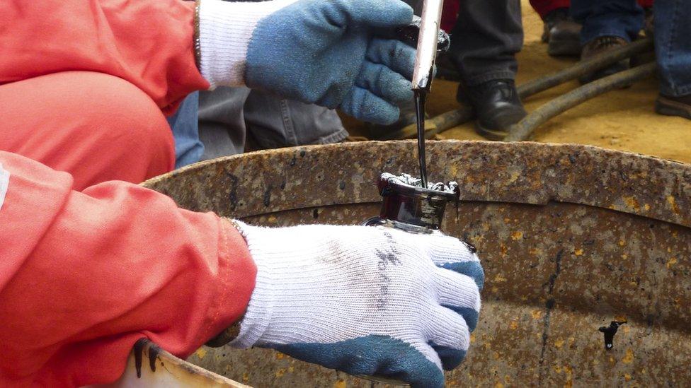 A technician takes an oil sample from a Venezuelan oil well