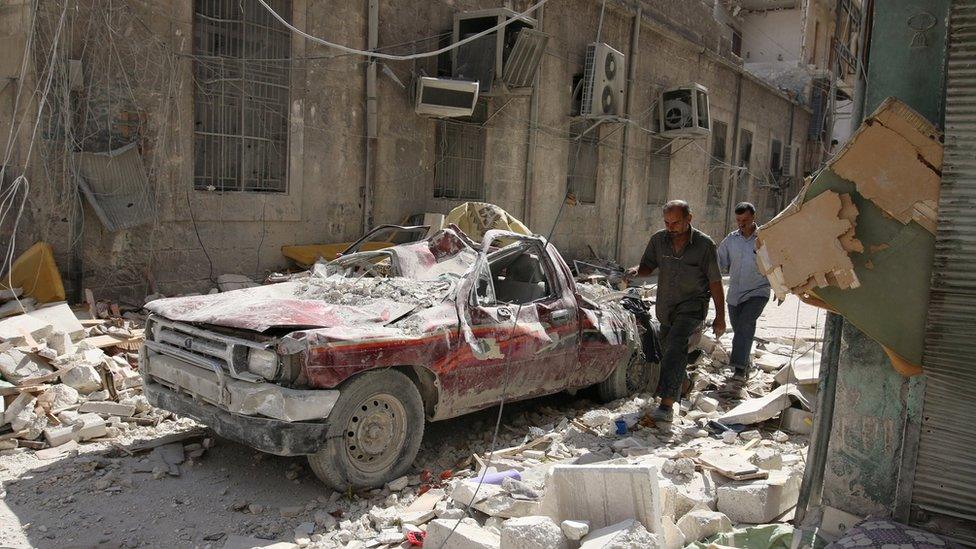 People walk near a damaged vehicle after an air strike Sunday in the rebel-held besieged al-Qaterji neighbourhood of Aleppo, Syria October 17, 2016