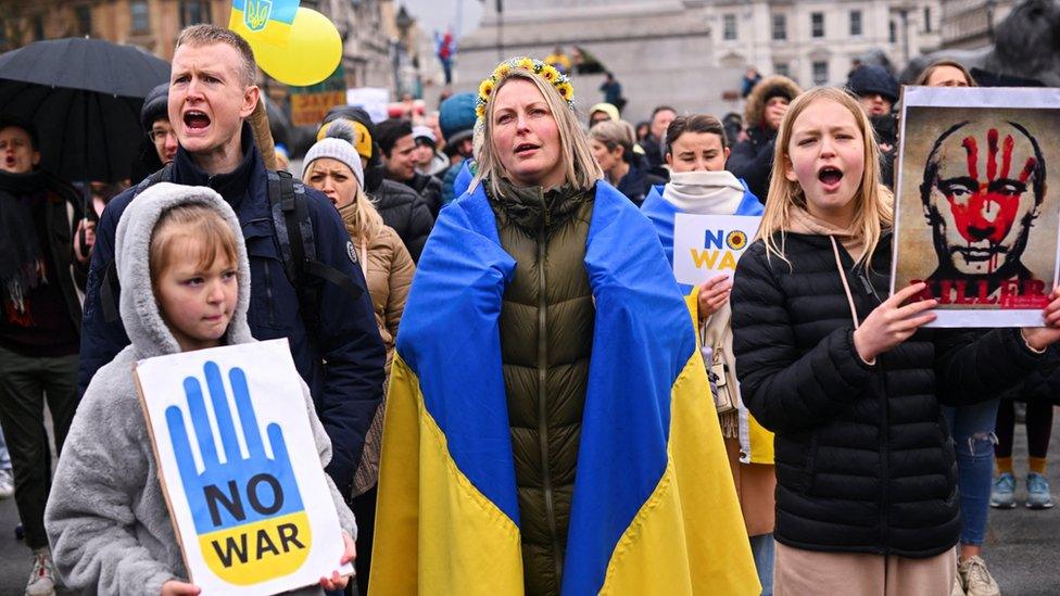 People hold banners - one depicting Russian President Vladimir Putin - as they take part in a protest against Russia's invasion of Ukraine