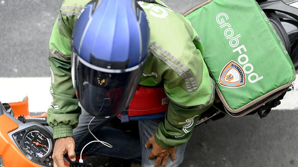 A Grab motorcycle rider checks his mobile phone in Bangkok, Thailand