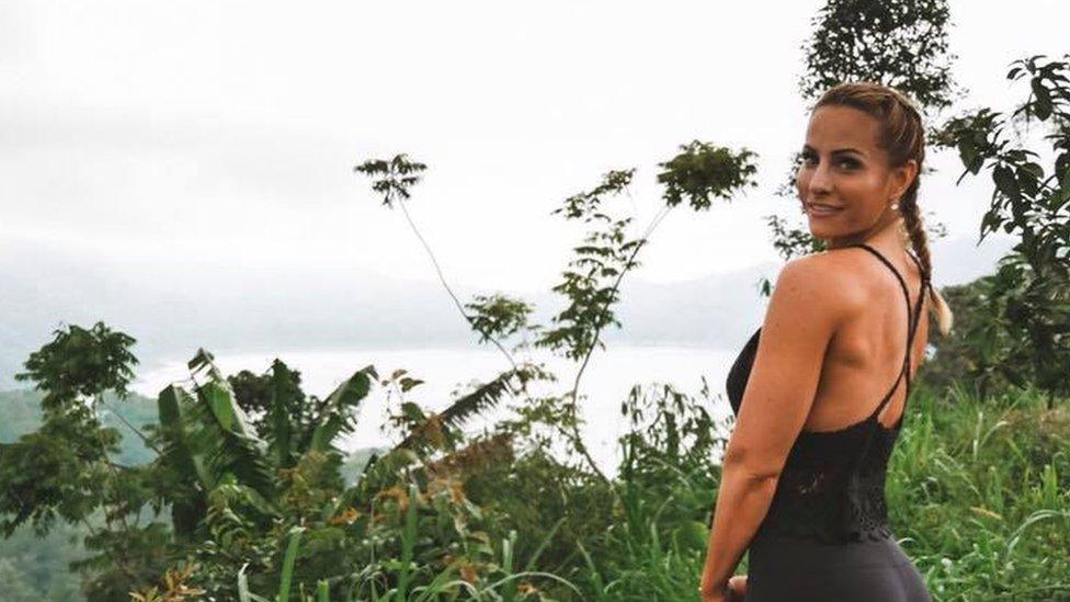 A photo of Rebecca Burger looking over her shoulder to the camera in front of some greenery