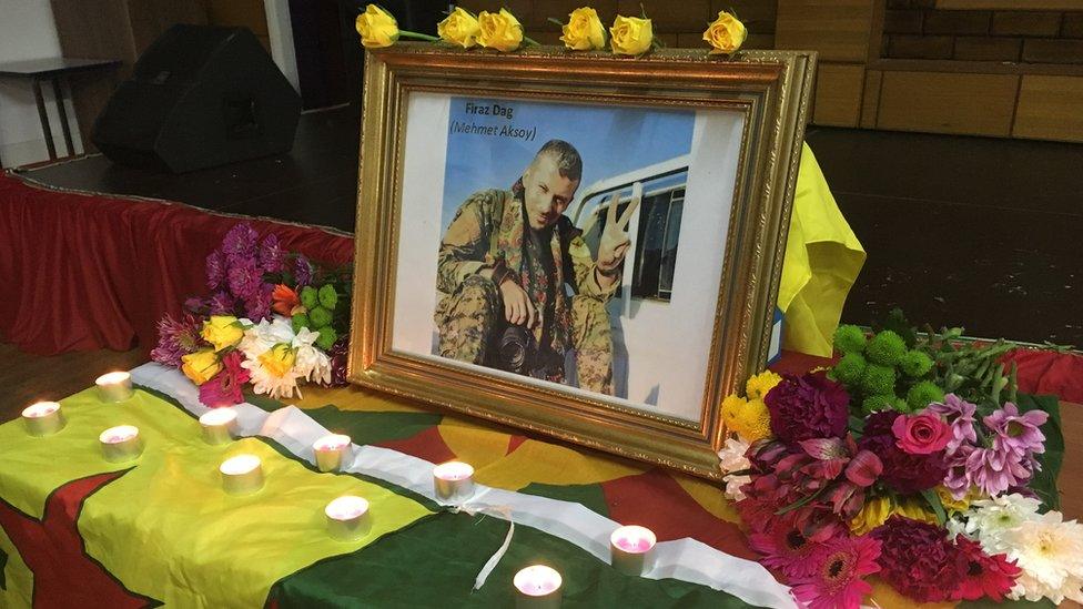 A photo of Mehmet Aksoy surrounded by flowers at his vigil