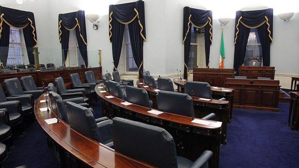 Irish senate - room with navy curtains and floor, curved tables with navy chairs in a row