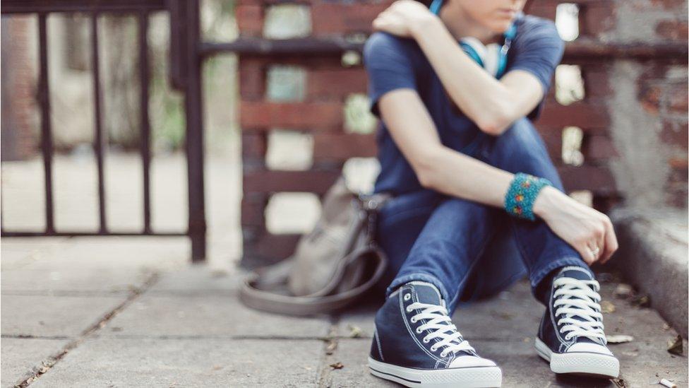 A person sits alone on the street. Their converse are visible in the foreground. They are quite blurry. The picture feels a bit lonely.