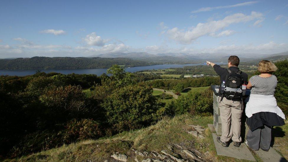 Visitors enjoying the view of Lake Windermere from the summit of Orrest Head, in the Lake District, Cumbria