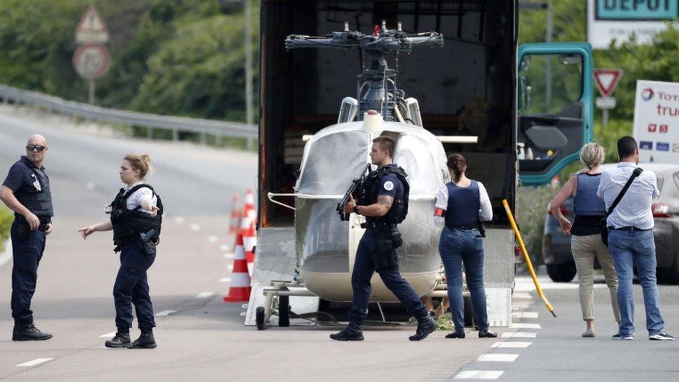 Armed police surround helicopter being loaded into a large vehicle