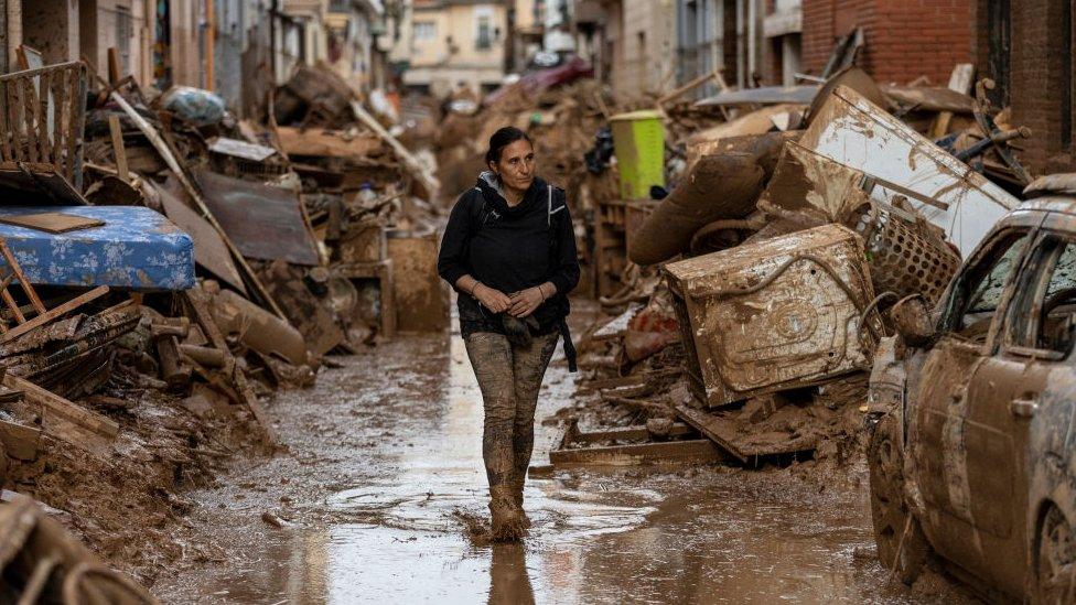 A woman covered in mud walks down a flooded street in Valencia