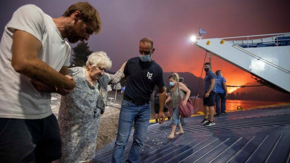 People board a ferry during evacuation as a wildfire burns in the village of Limni, on the island of Evia