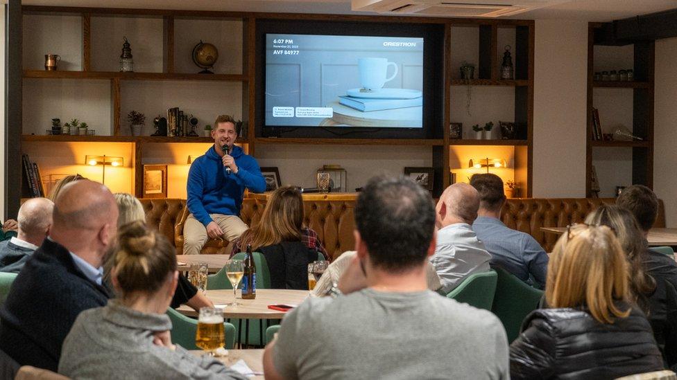 A group of people listening to a man on a chair