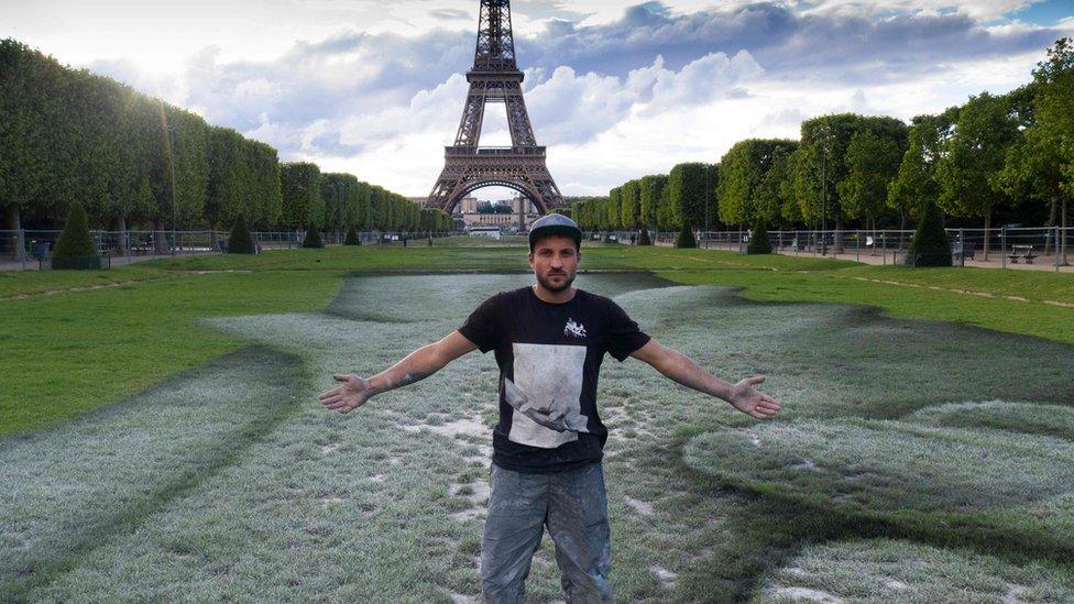 French street artist Saype poses at the Eiffel Tower in front of his giant artwork "Beyond Walls"